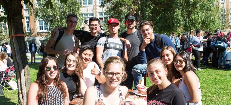 A group of young people sitting outside around a picnic table and smiling for the camera.