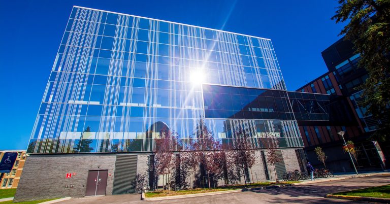 University building with a glass facade, with the sun shining on it.