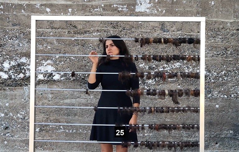 A woman standing behind an abacus-like structure with rolls of hair instead of beads.