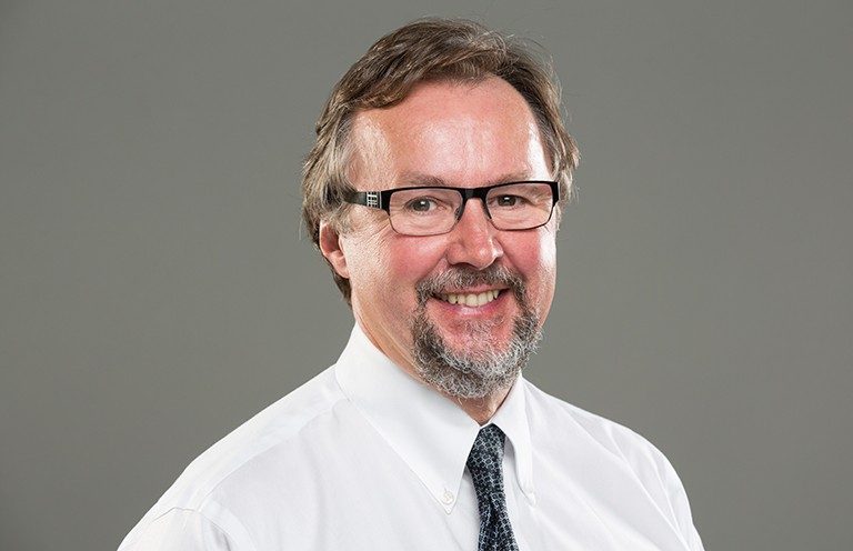 Middle-aged smiling man with glasses, a beard and a white shirt.