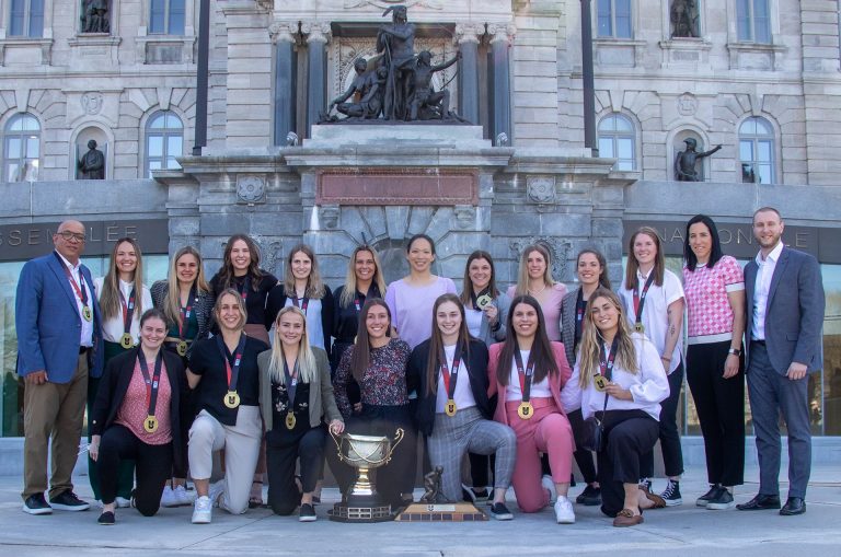 A women's sport team wearing gold medals, photographed in front of government buildings.