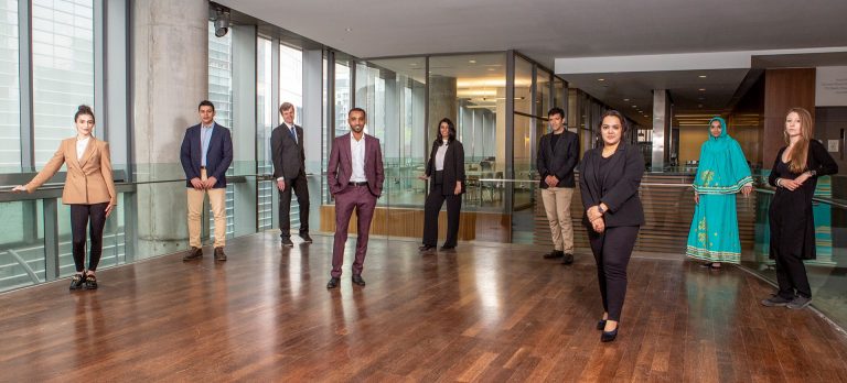 A group of diverse people standing together but spaced apart and looking at the camera.