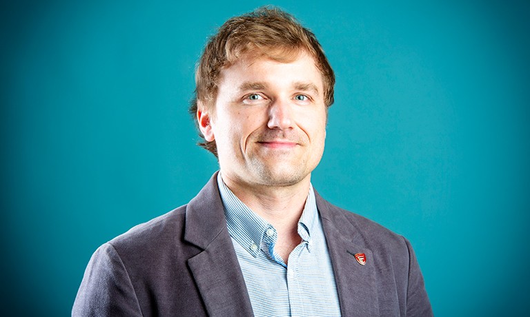 Smiling man with short(ish) blonde hair and a checkered collared shirt.