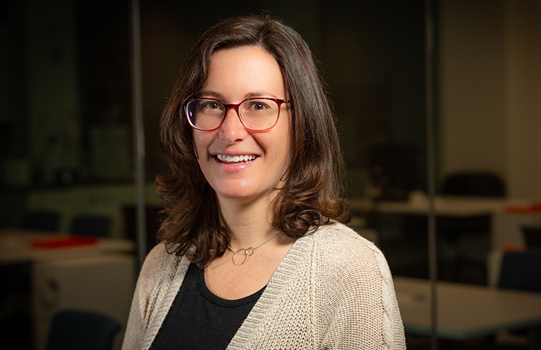 Ashlee Howarth: “It’s great for our students to gain hands-on experience with new equipment.” Young smiling woman with dark, long hair, glasses, a black T-Shirt and beige cardigan.