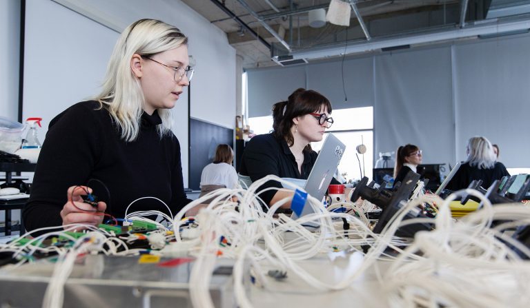 Two women in a university research lab, with computers and wires on the table.