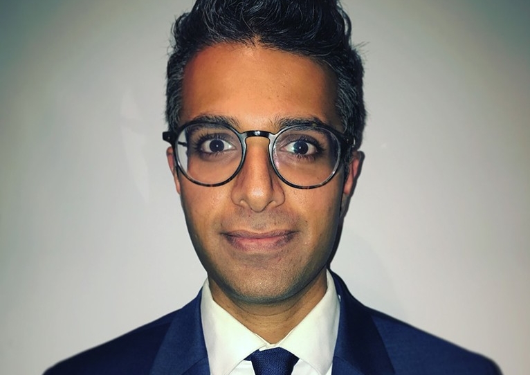 Young man with dark brown eyes, black hair, a blue tie, white shirt and blue suit jacket.