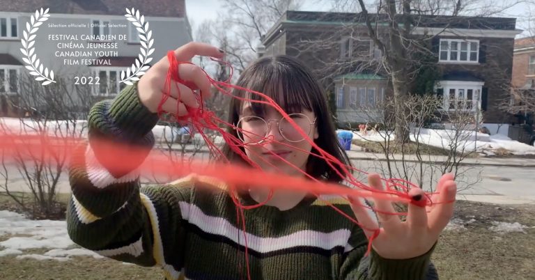 Young woman with shoulder-length brown hair and round glasses holding red yarn in her fingers