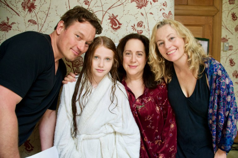 Group shot of man in black t-shirt, girl in white bathrobe, woman in burgundy patterned blouse and woman with black dress and open blue blouse
