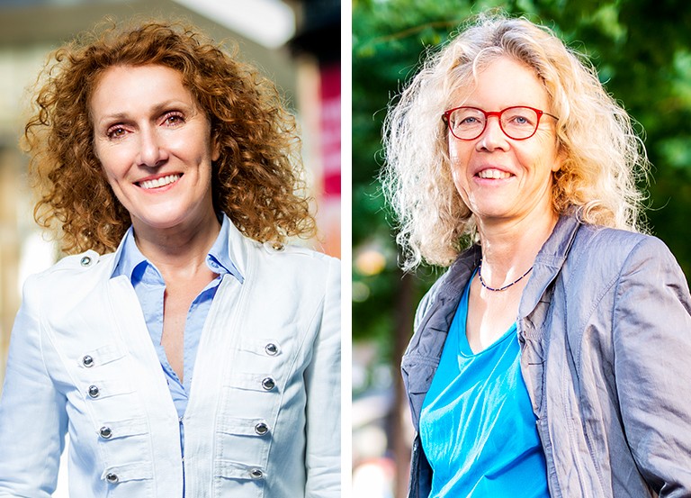 On the left, a smiling woman with long, curly, red hair, wearing a white jacket and blue shirt. On the right, a smiling woman with long, curly, blonde hair, wearing red-rimmed glasses, a grey jacket and a blue top.