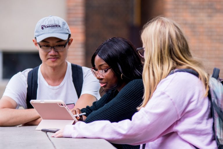 3 students talking at a picnic table with tablet in front of them