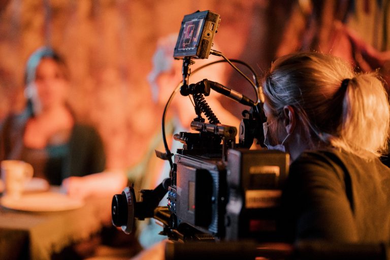 A young woman with brown hair looks down into the viewfinder of a large film camera.