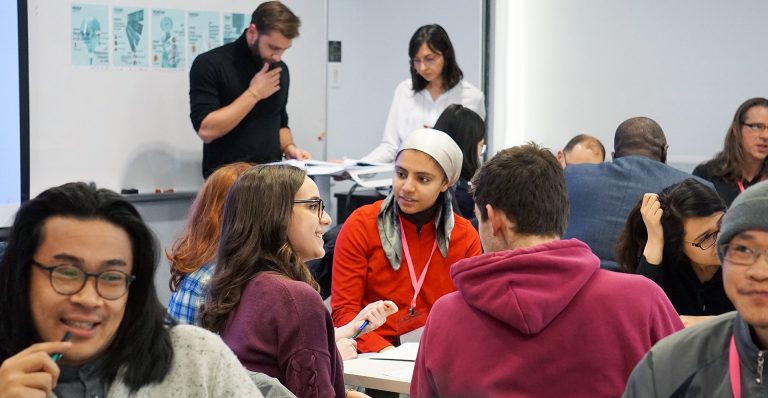 A group of young people in a university classroom environment talking together.