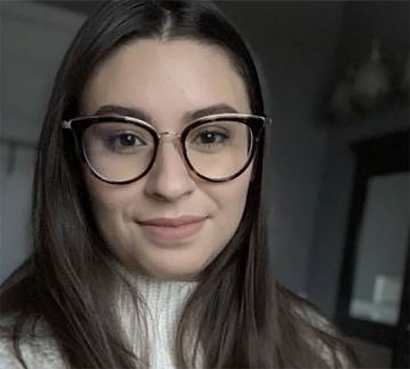 Young, smiling woman with long dark, hair and black-rimmed glasses