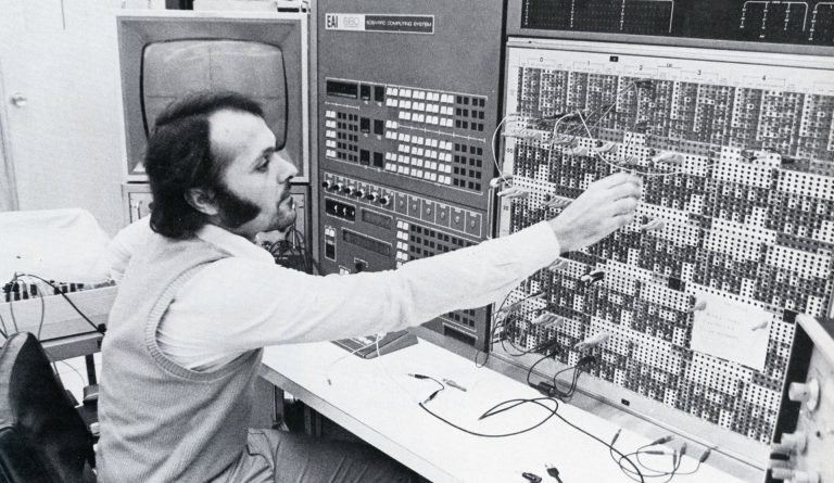 A black-and-white archive photo of a man with black hair and sideburns, using a switchboard