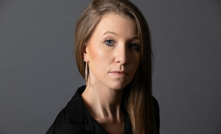 A serious-looking White woman with long blonde hair, wearing a black shirt.