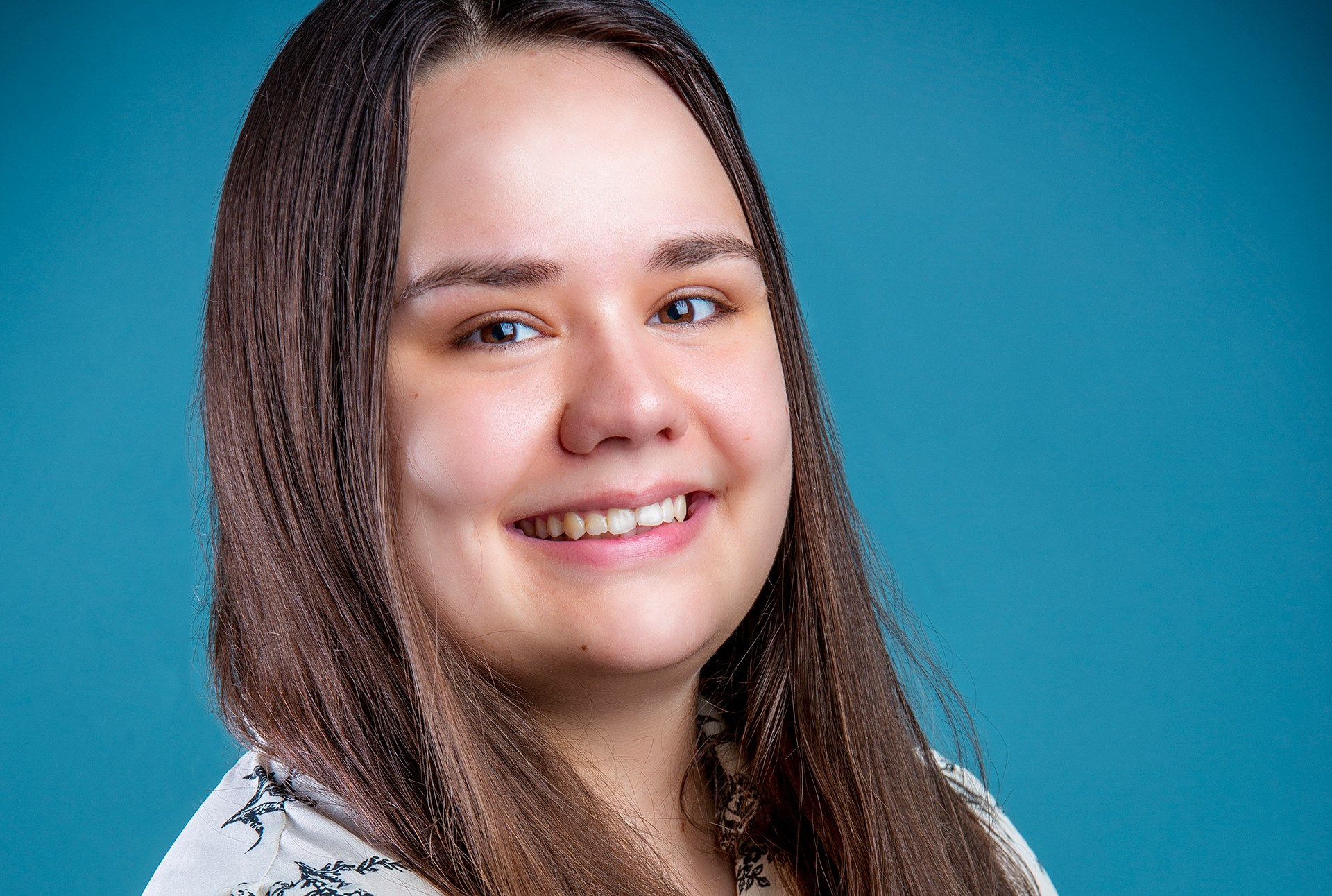 Smiling woman with long, straight, brown hair, and wearing a patterned shirt.