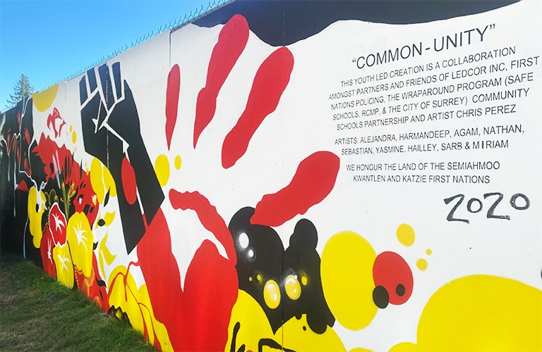 The community action project’s mural in B.C. displays Indigenous medicine wheel colours and the Black Lives Matter fist next to a red hand representing missing and murdered Indigenous women. Mural with graphic depictions of hand and flowers and a text with the heading "Common - Unity"