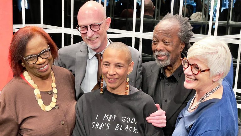 A group of five people  — two men and three women — standing together and smiling for a camera off to the left.