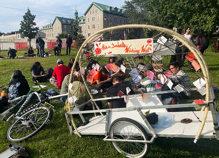 Young people sitting on a grassy field with a wheeled contraption in the foreground.