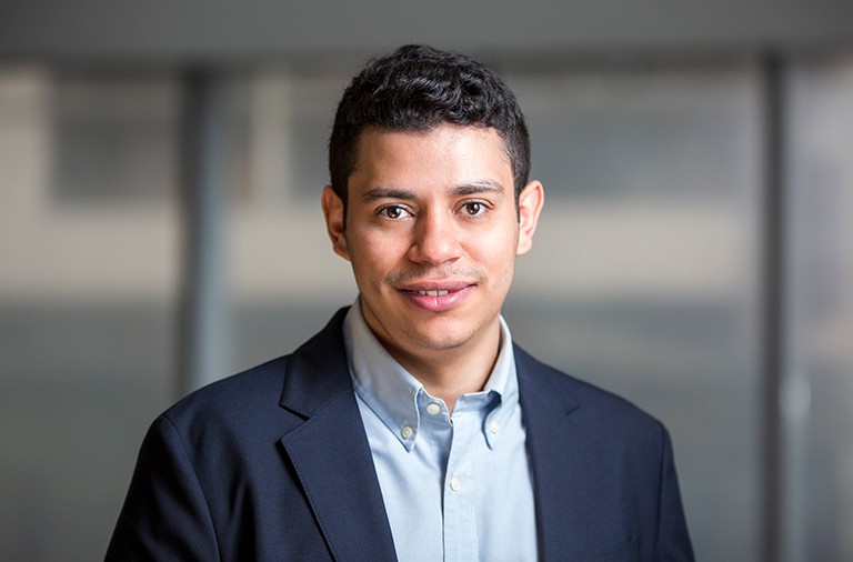 Young man with short, dark hair and wearing a light-blue shirt and navy blue suit jacket.