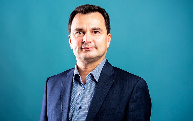 Man with short, dark hair and wearing a blue blazer and light-blue shirt.