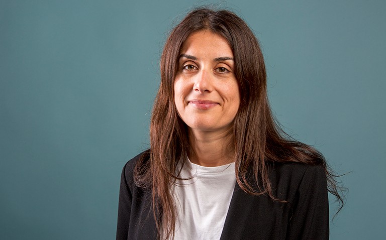 Woman with long brown hair, wearing a black blazer and a white T-shirt.