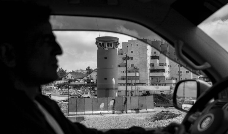 Profile view of a man in silhouette driving a car in an urban setting.