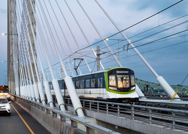 A lightrail train running across tracks on a bridge with a city in the background.