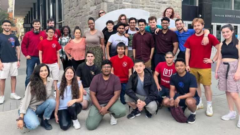 A group of young people standing or kneeling outside and smiling for the camera.