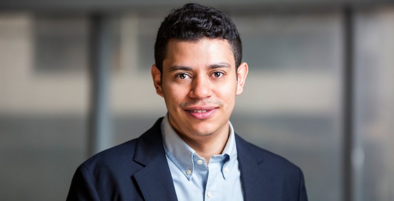 Smiling young man with short, dark hair and wearing a blue dress shirt and dark blue blazer.