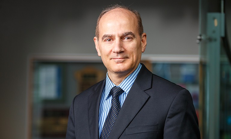 Slightly smiling balding man wearing a dark suit and tie and blue dress shirt.