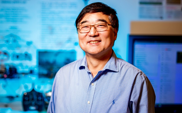 Smiling man with glasses, wearing a blue shirt and in a lab environment.