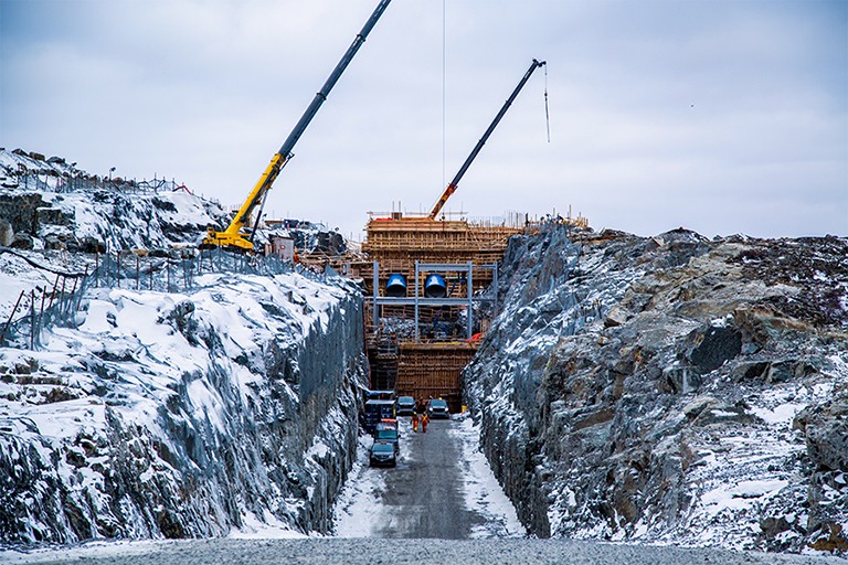 A construction site where a dam is being built between two walls of rock covered in snow, where once a river ran.