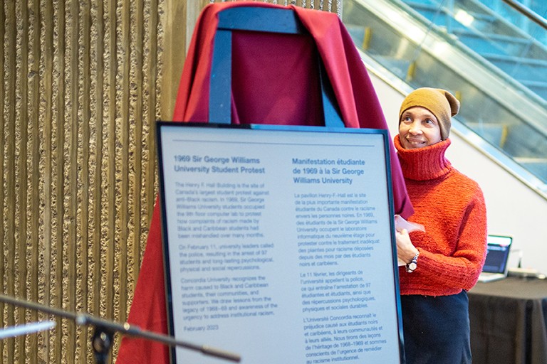 A smiling woman in a yellow beanie unveils a commemorative plaque.