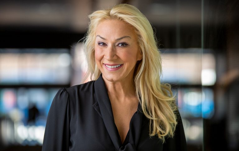 Smiling woman with long, blonde hair and wearing a black chiffon top.