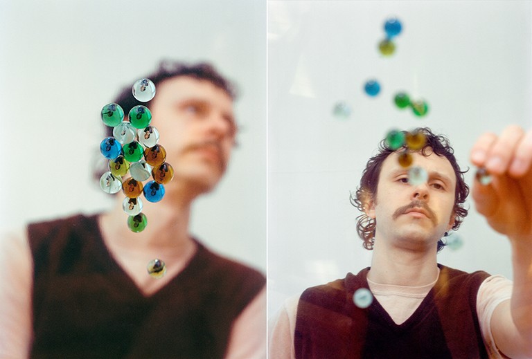 A diptych image of two portraits of the same young man with light brown, curly hair and a moustache, with the left image blurry, while the right image is in focus