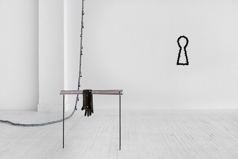 “Muscle Worn & Wearing” by Kyle Alden Martens, 2022. Circa Art Actuel, Montreal. | Documentation by Jean-Michael Seminaro A white gallery space, with a rope snaking in from the left and a stand with one empty glove hanging on it, while a large sculpture like a keyhole hangs on the wall.