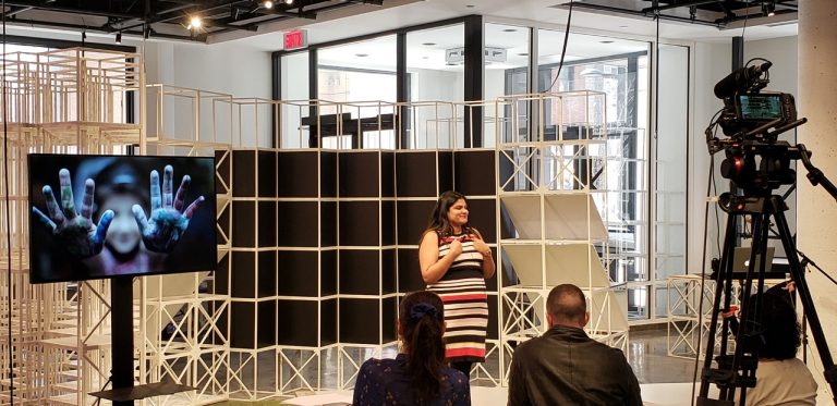 Woman in striped dress presenting to an audience and in front of a camera