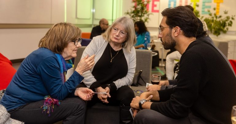 Two men and a woman sit at a low table in a discussion during an event