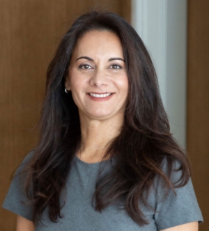 Smiling woman with long, dark hair and wearing a grey short-sleeved top.