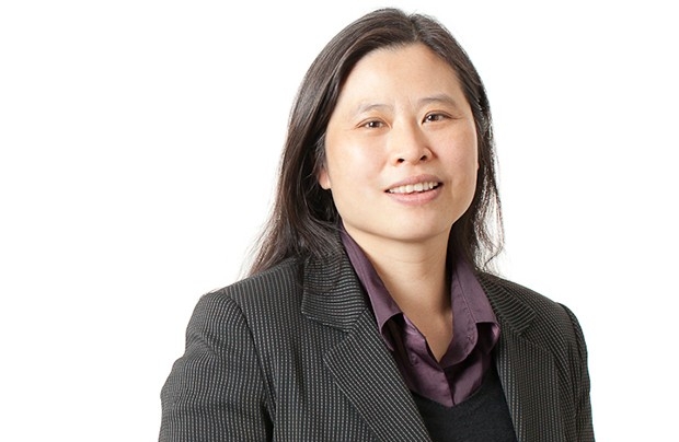 Smiling woman with long, dark hair, wearing a burgundy shirt and a brown blazer