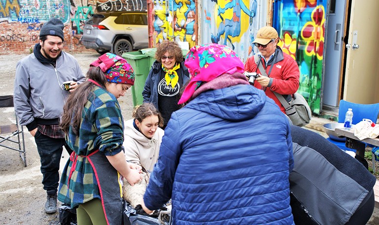 A group of people standing around a table, smiling and working on something that we can't see.