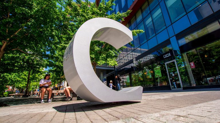 A city boulevard with cobblestone pavings and a large statue of the letter "C."