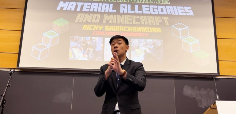 A young man in a brown suit speaking into a microphone at a presentation.