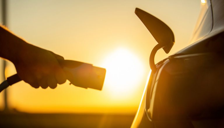 Image of a person's hand putting a charger into an electric car at sunset