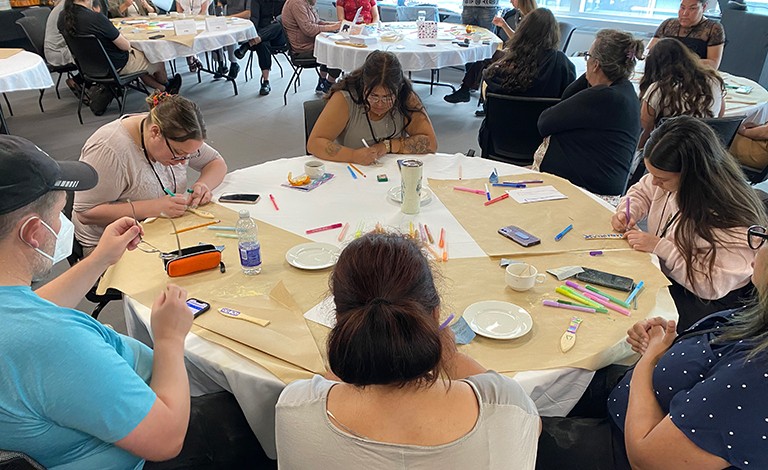 Participants make paddles to reconnect and create. Groups of people sitting at round tables, making arts and crafts.