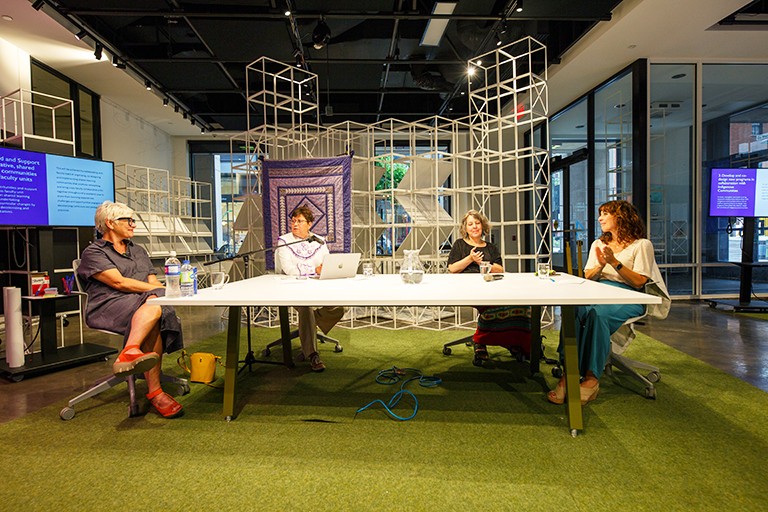 Four women sitting around a large table in an interior setting.