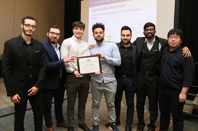 A group of young men in suits smiling for the camera, with the two in the middle of the group holding an award plaque