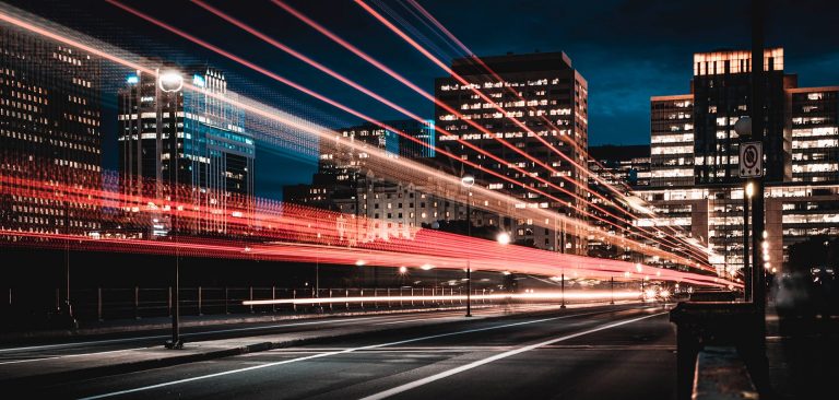 A city at night, with the long exposure light tails from a retreating train