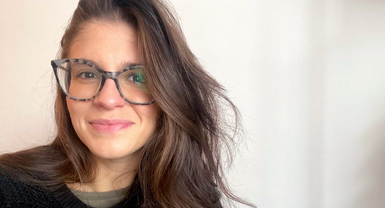 Young smiling woman with long, dark brown hair, wearing glasses and a black top.